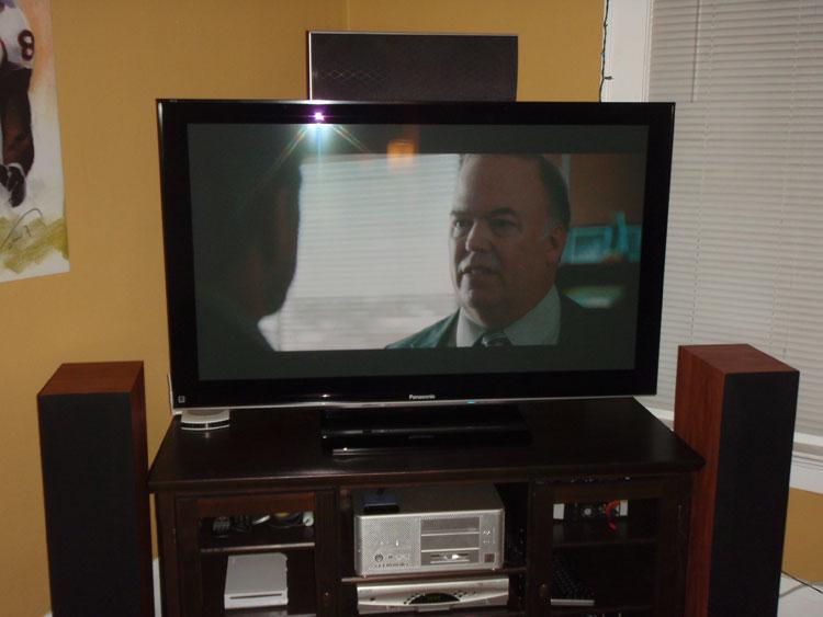 A flat screen television with a center channel speaker mounted above it